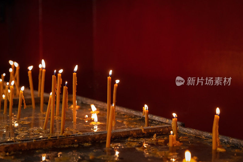 Lit thin wax candles standing in candleholders on church table against a red wall, religion concept